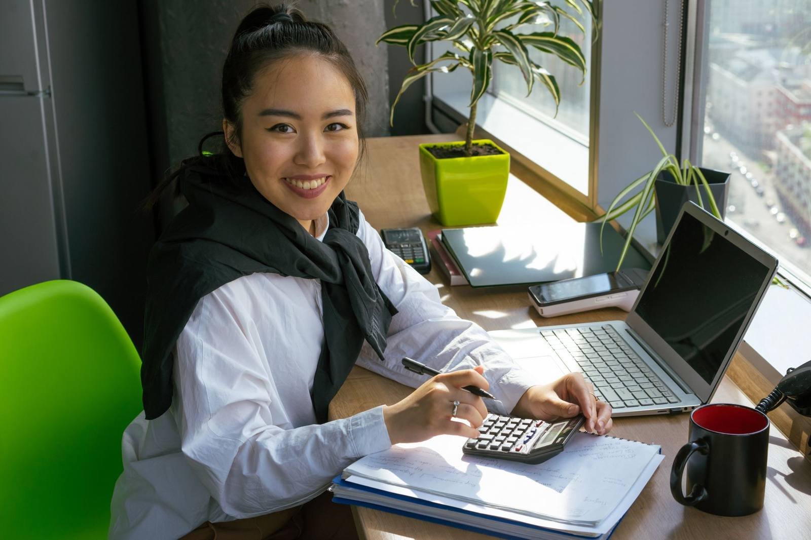 UK accountant smiling at her desk with a calculator and laptop in a bright office