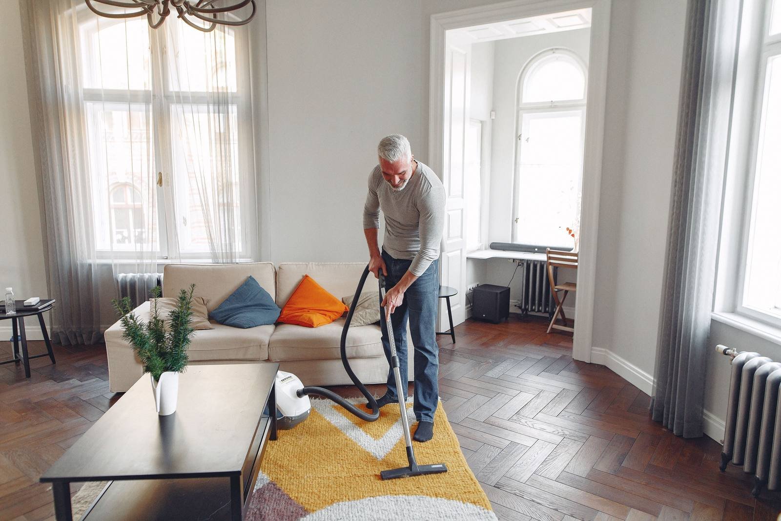 Man vacuuming a rug in a bright living room