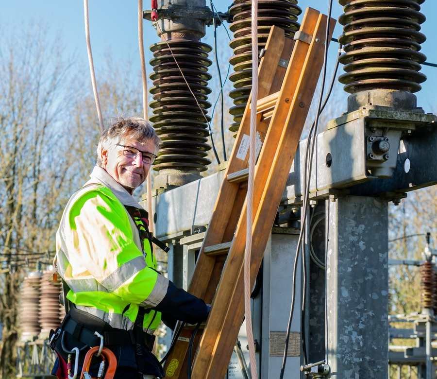 UK electrician in hi-vis smiling at an outdoor substation