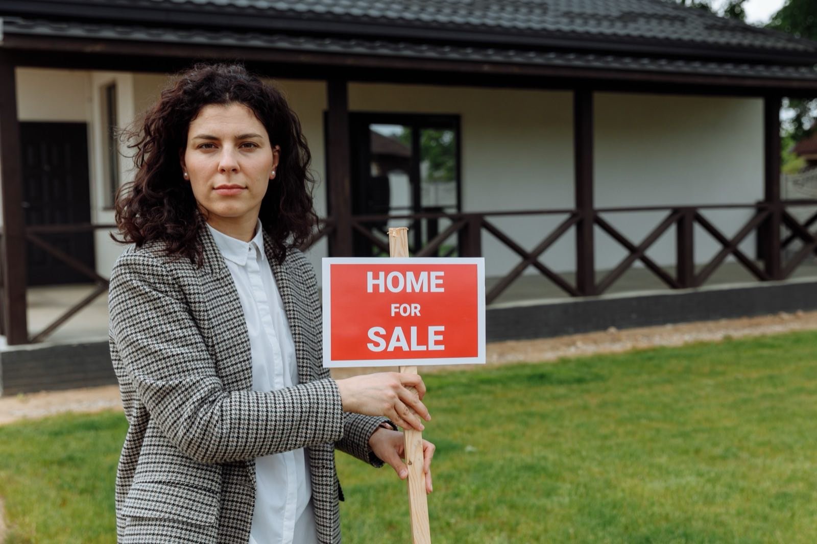 UK estate agent standing outside a house holding a Home For Sale sign
