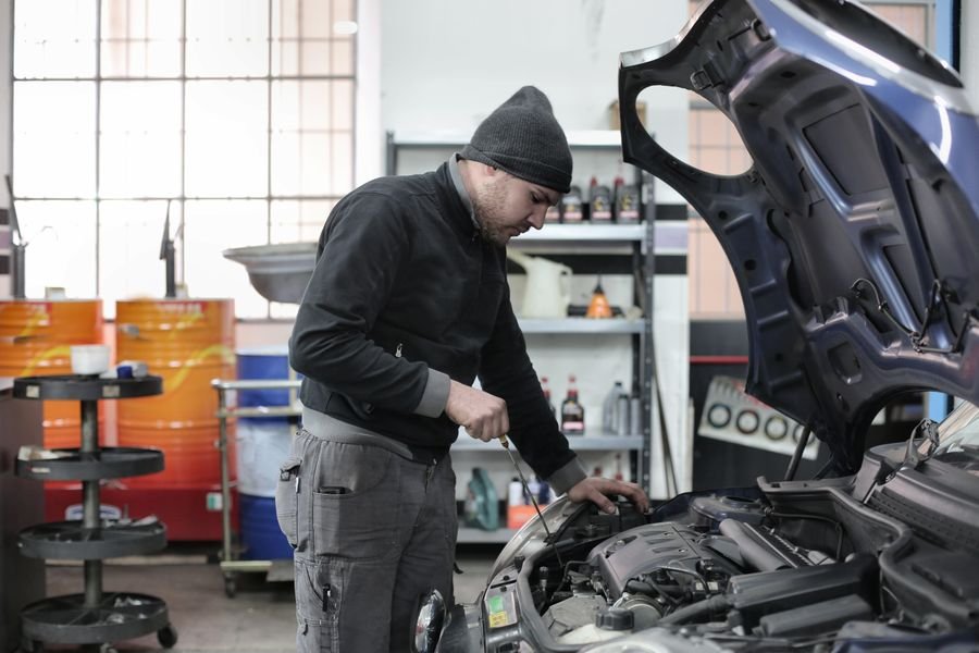 UK mechanic checking an engine under the bonnet in a busy car workshop