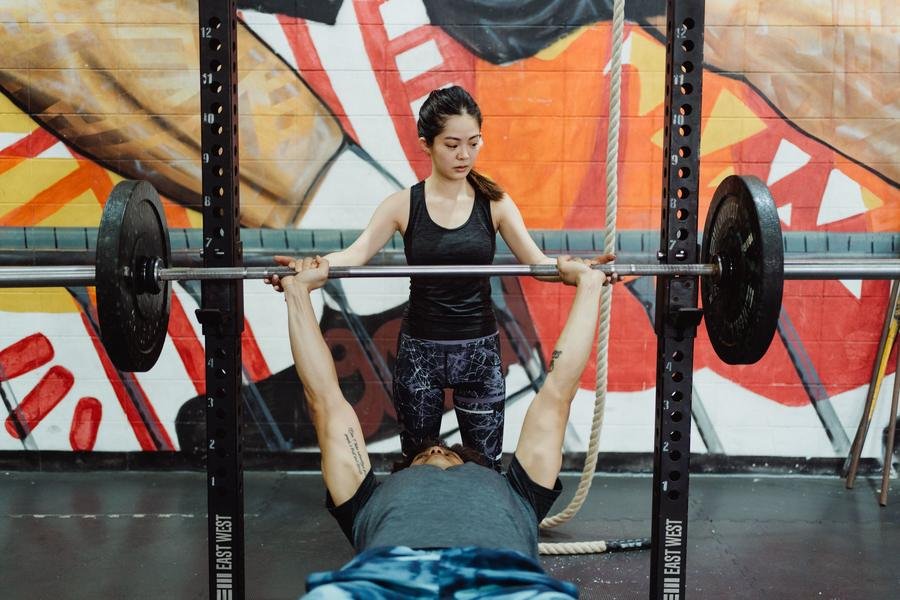 UK personal trainer spotting a client on a bench press in a gym