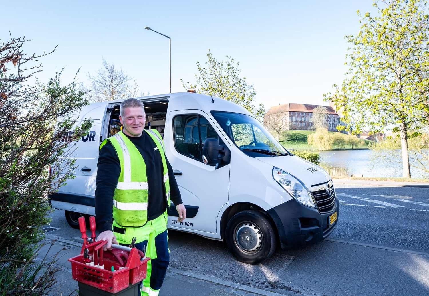 UK heating and air-conditioning engineer in a hi-vis vest smiling by his work van with a toolbox