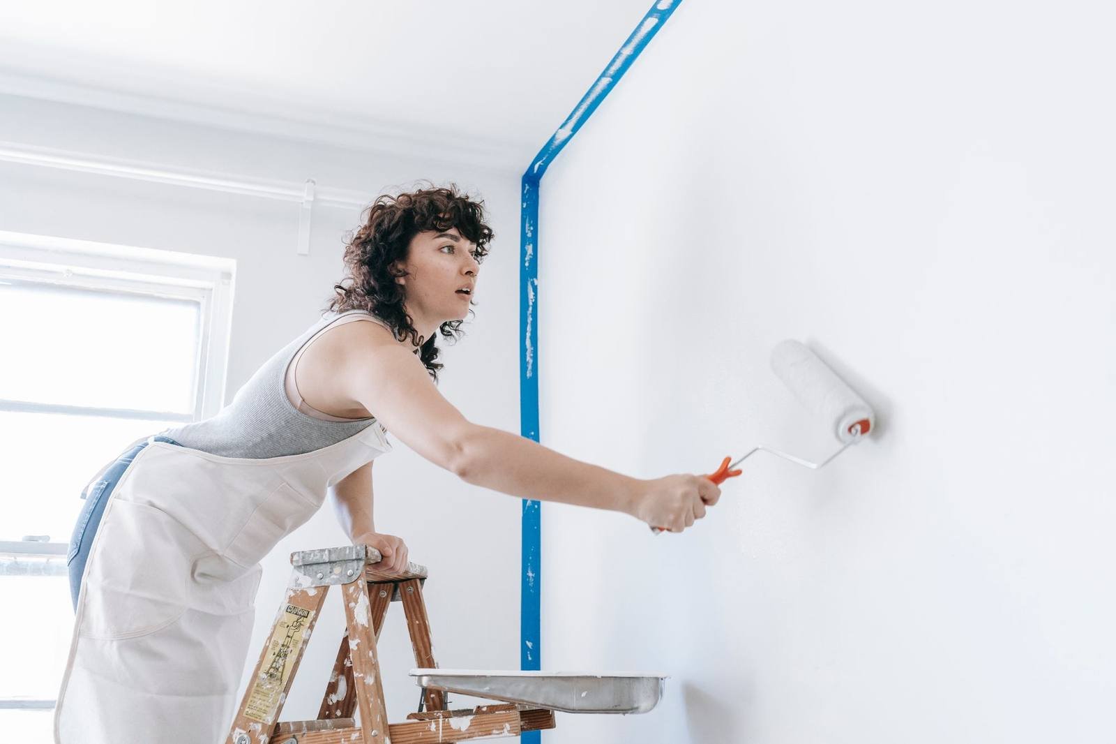 UK painter and decorator taping and rolling paint onto an interior wall