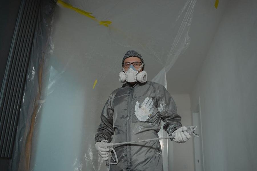 Pest control technician in full protective gear spraying treatment inside a property