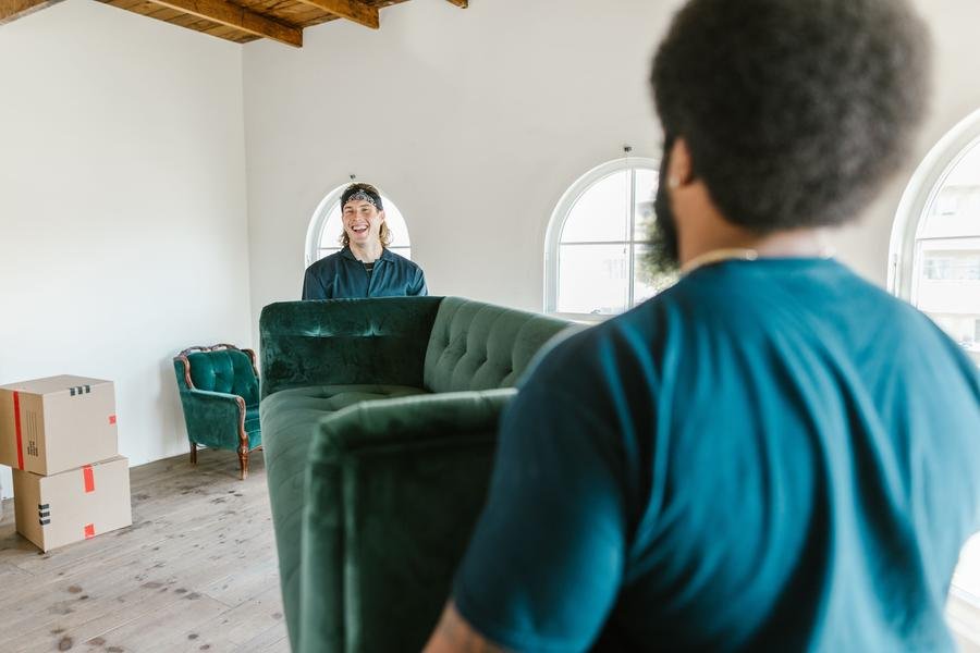 Two UK removals workers carrying a sofa into a home