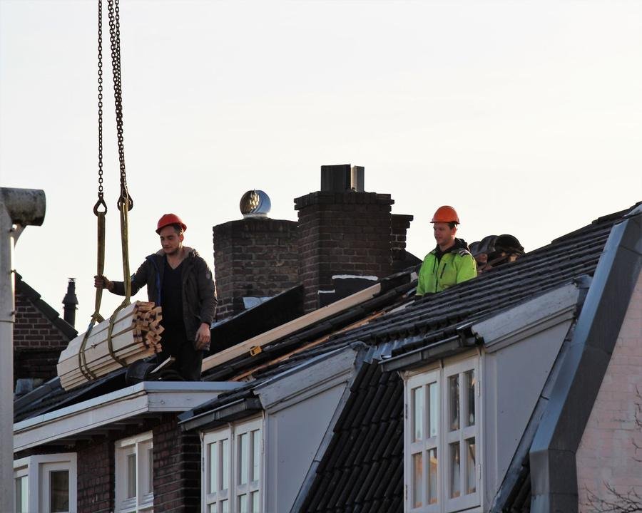 Two UK roofers in hard hats working on a terraced house roof