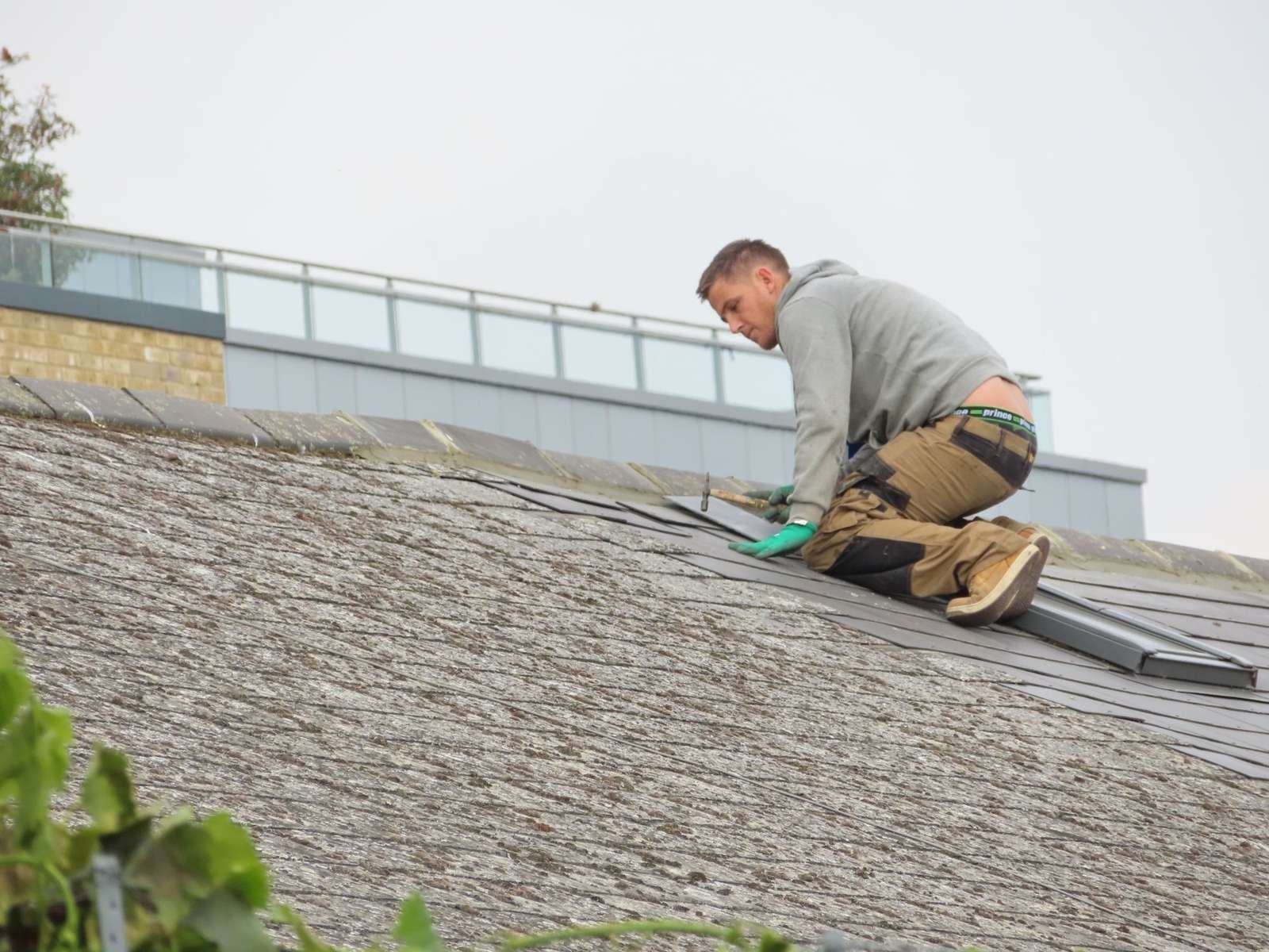 UK roofer kneeling on a slate roof carrying out a repair